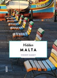 Row of multicolored slated wood chairs, near harbour edge, with boat, on cover of Hidden Malta', by Luster Publishing.