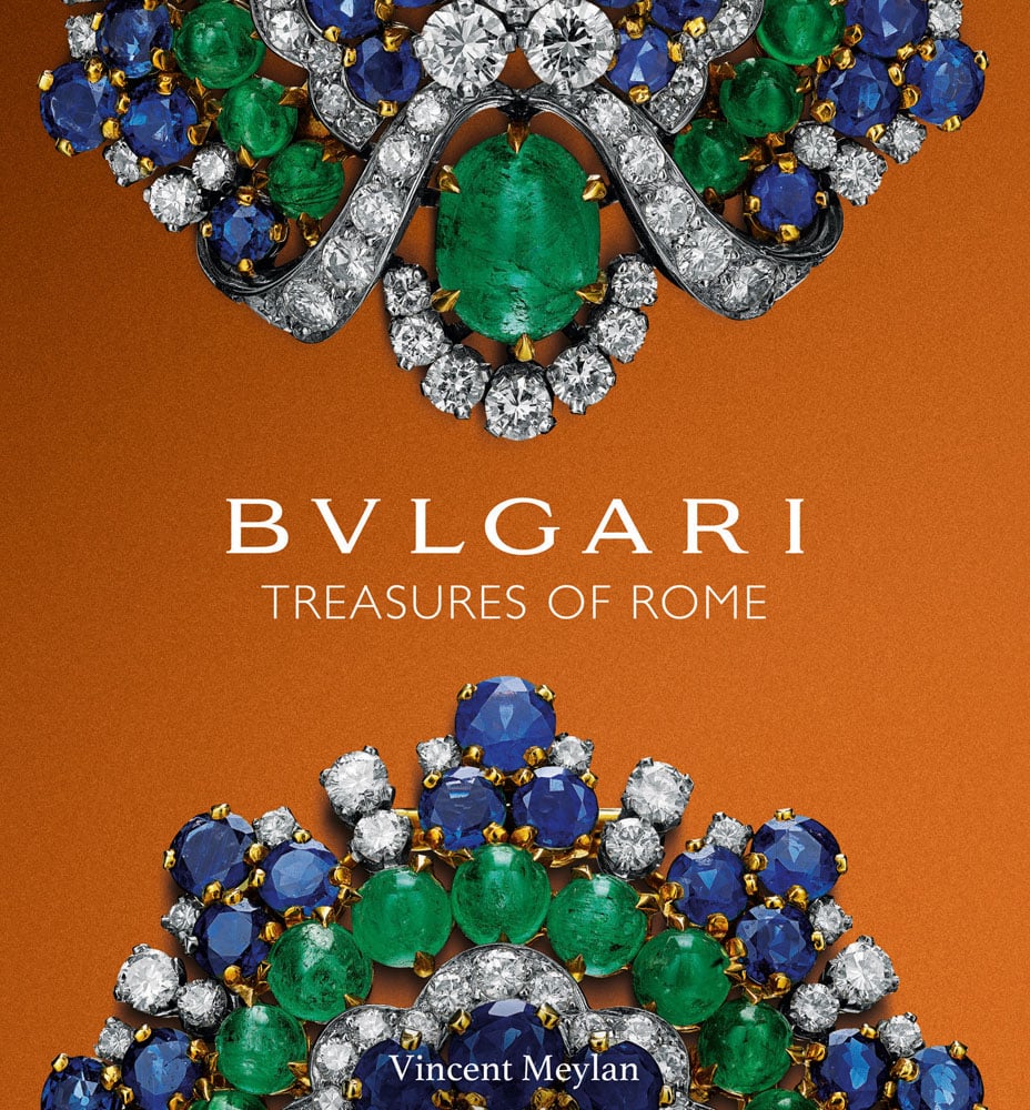 Two halves of sapphire and emerald gemstones encrusted jewellery, on orange cover of 'Bulgari Treasures of Rome', by ACC Art Books.