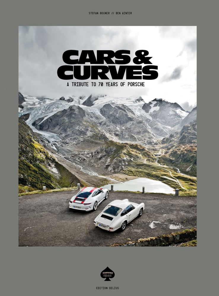 Two white Porsche models parked on mountain roadside, on grey cover of 'Cars & Curves, A Tribute to 70 Years of Porsche', by Delius Klasing.