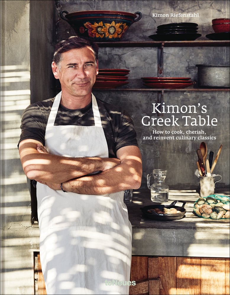 Kimon Riefenstahl in white apron, standing in kitchen, 'Kimon’s Greek Table', in white font to centre right of cover, by teNeues Books.