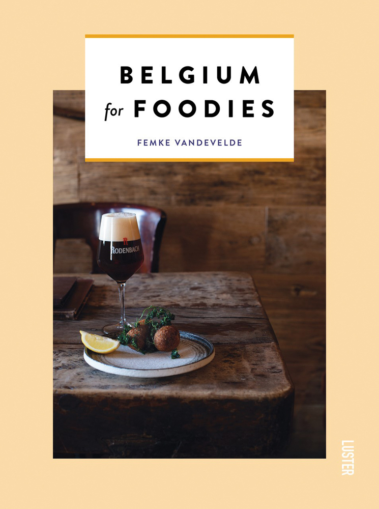 Plate of fried food with kale and lemon slice, glass of beer on walnut table, on cover of 'Belgium for Foodies', by Luster Publishing.