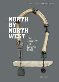 Long jewelry piece made of wooden tube shapes, and dark metal pendants on grey cover of 'North by Northwest, The Jewelry of Laurie Hall', by Arnoldsche Art Publishers.