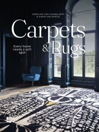 Living interior with navy wall paneling, large black and white rug, arch windows, on cover of 'Carpets & Rugs, Every home needs a soft spot', by Lannoo Publishers.