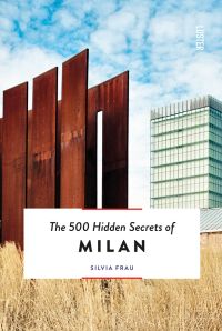 Tall rusted metal panelled structure surrounded by pale dry grass, tall building behind, on cover of 'The 500 Hidden Secrets of Milan', by Luster Publishing.