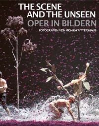 Opera theater production, three windswept figures with water splashing at feet, tree to left, pink confetti in air, on cover of 'The Scene and the Unseen, Opera in Pictures. Photographs by Monika Rittershaus, by Arnoldsche Art Publishers.