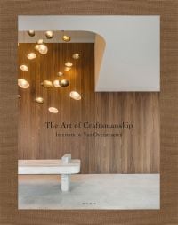 Interior with wood panelled wall, low hanging modern light fitting, marble seat, on cover of 'The Art of Craftsmanship, Interiors by Van Overstraeten', by Beta-Plus