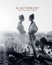 Book cover Liam Bailey's Glastonbury: The Festival and Its People, with festival goers standing at top of hill with tents behind them. Published by ACC Art Books.