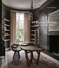 Book cover of Curated Living: Elegant Interiors and Artful Homes, featuring an interior living room with wood table and beige drapes. Published by Images Publishing.