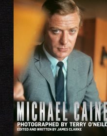 Book cover of 'Michael Caine, Photographed by Terry O'Neill, featuring the actor staring seriously at the camera, from the 1966 film 'Funeral in Berlin'. Published by ACC Art Books.