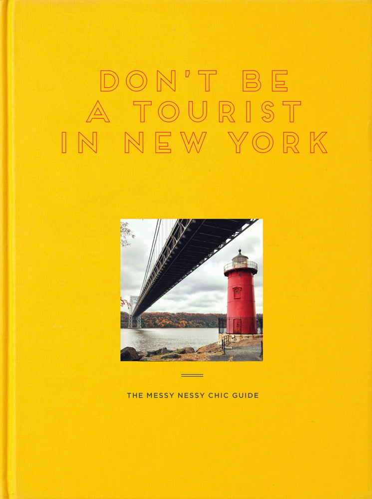 Yellow book cover of Don't Be a Tourist in New York, with a little red lighthouse under great grey bridge on Hudson River. Published by 13 Things Ltd.