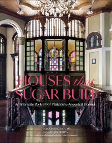 Grand interior with dark wood staircase, chandelier and stained glass interior windows, on cover of 'Houses that Sugar Built, An Intimate Portrait of Philippine Ancestral Homes', by ORO Editions.