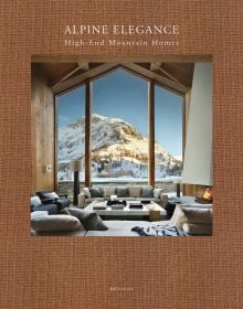 Book cover of Alpine Elegance: High-End Mountain Homes, featuring a cosy house with a view of snow topped mountains through the large windows. Published by Beta-Plus.