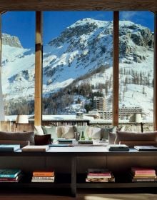 Book cover of Alpine Elegance: High-End Mountain Homes, featuring a cosy house with a view of snow topped mountains through the large windows. Published by Beta-Plus.