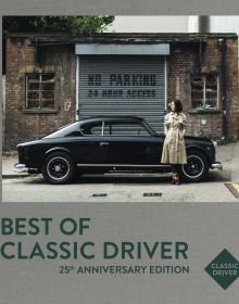 Mai Ikuzawa in beige trench coat, standing next to black Lancia Aurelia B20 GT, on grey linen cover of 'Best of Classic Driver, 25th Anniversary Edition', by Delius Klasing Verlag.