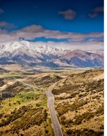 Book cover of Stefan Bogner's CURVES New Zealand: Volume 22, with a winding road on the coast, with snow covered mountains behind. Published by Delius Klasing.