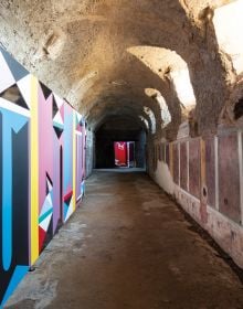 Installation wall with red, black, white, blue triangle shape patterns, Catrin Huber in white font to centre left