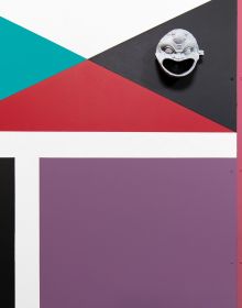 Installation wall with red, black, white, blue triangle shape patterns, Catrin Huber in white font to centre left