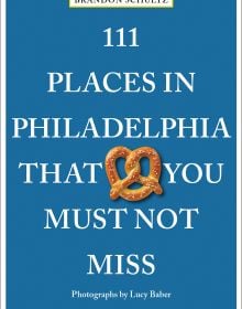 Pretzel near center of blue cover of '111 Places in Philadelphia That You Must Not Miss', by Emons Verlag.