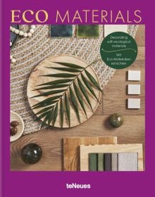 Aerial view of wood floor with woven rug, wooden plate with green palm leaf, on purple cover of 'Eco Materials, Decorating with Ecological Materials', by teNeues Books.