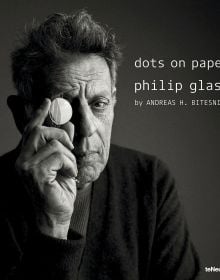 Book cover of dots on paper, Philip Glass by Andreas H. Bitesnich, with the composer in dark jacket, holding circular piece of glass to right eye. Published by teNeues Books.