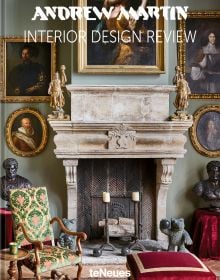 Interior living room of La Maison Semonville with stone fireplace, framed paintings and plush furniture, on cover of 'Andrew Martin Interior Design Review Vol. 27', by teNeues Books.