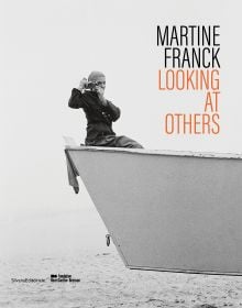 Book cover of Martine Franck: Looking at Others, with the photographer sitting in a skip while taking a photograph of the viewer. Published by Silvana.