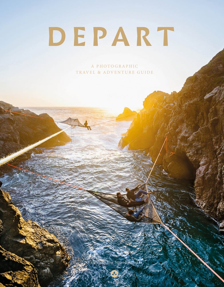 High angle view down onto seascape with 3 figures laying in hammock fixed to surrounding rocks, on cover of 'Depart, A photographic travel & adventure guide', by Lannoo Publishers.