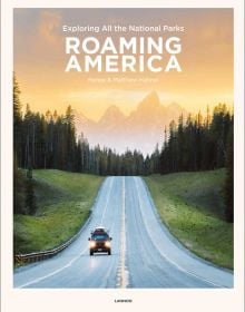 Campervan on straight road with mountainous landscape behind and orange sky, on cover of 'Roaming America, Exploring All the National Parks', by Lannoo Publishers.